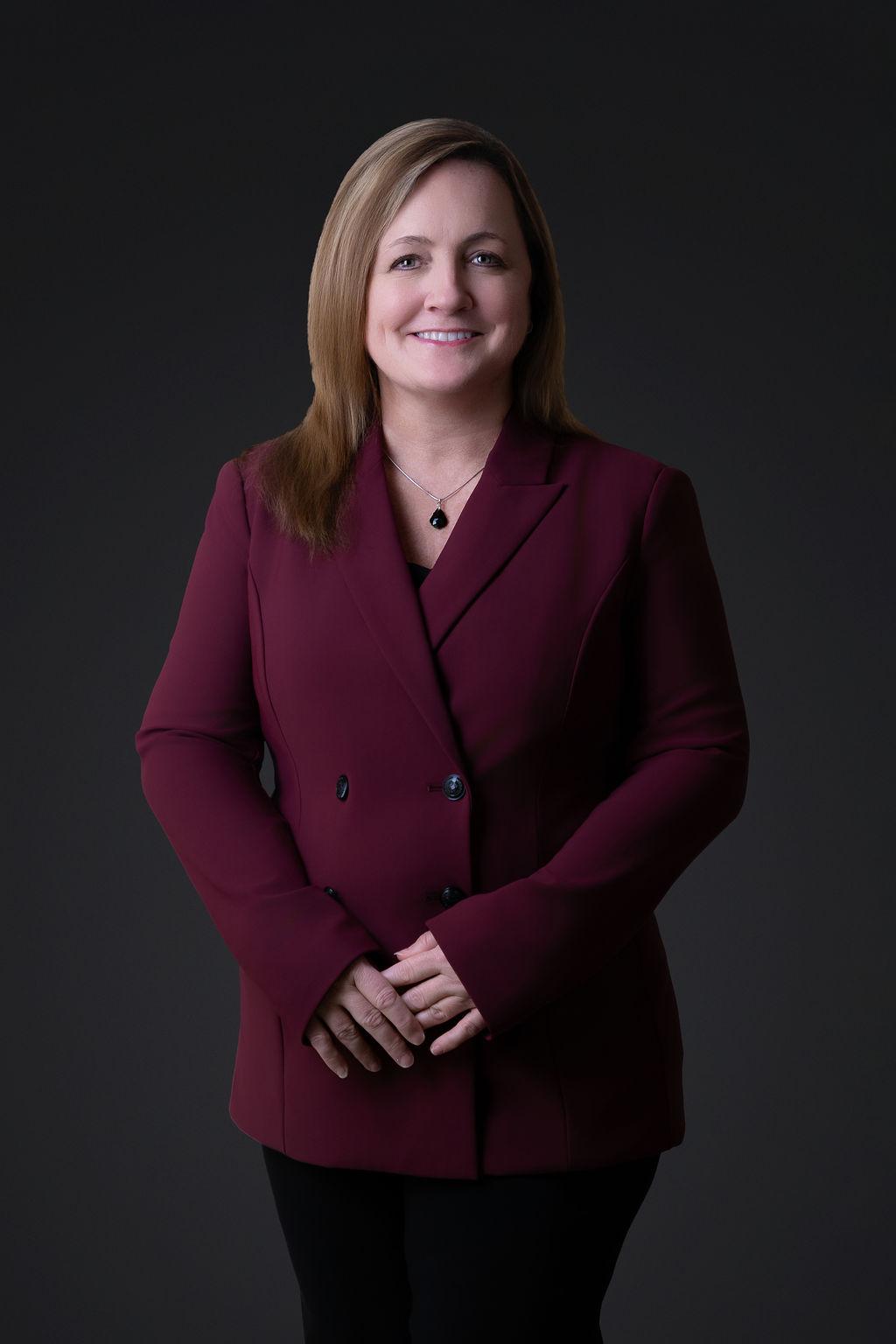 Portrait of Lesley Clack with dark hair wearing a maroon blazer.